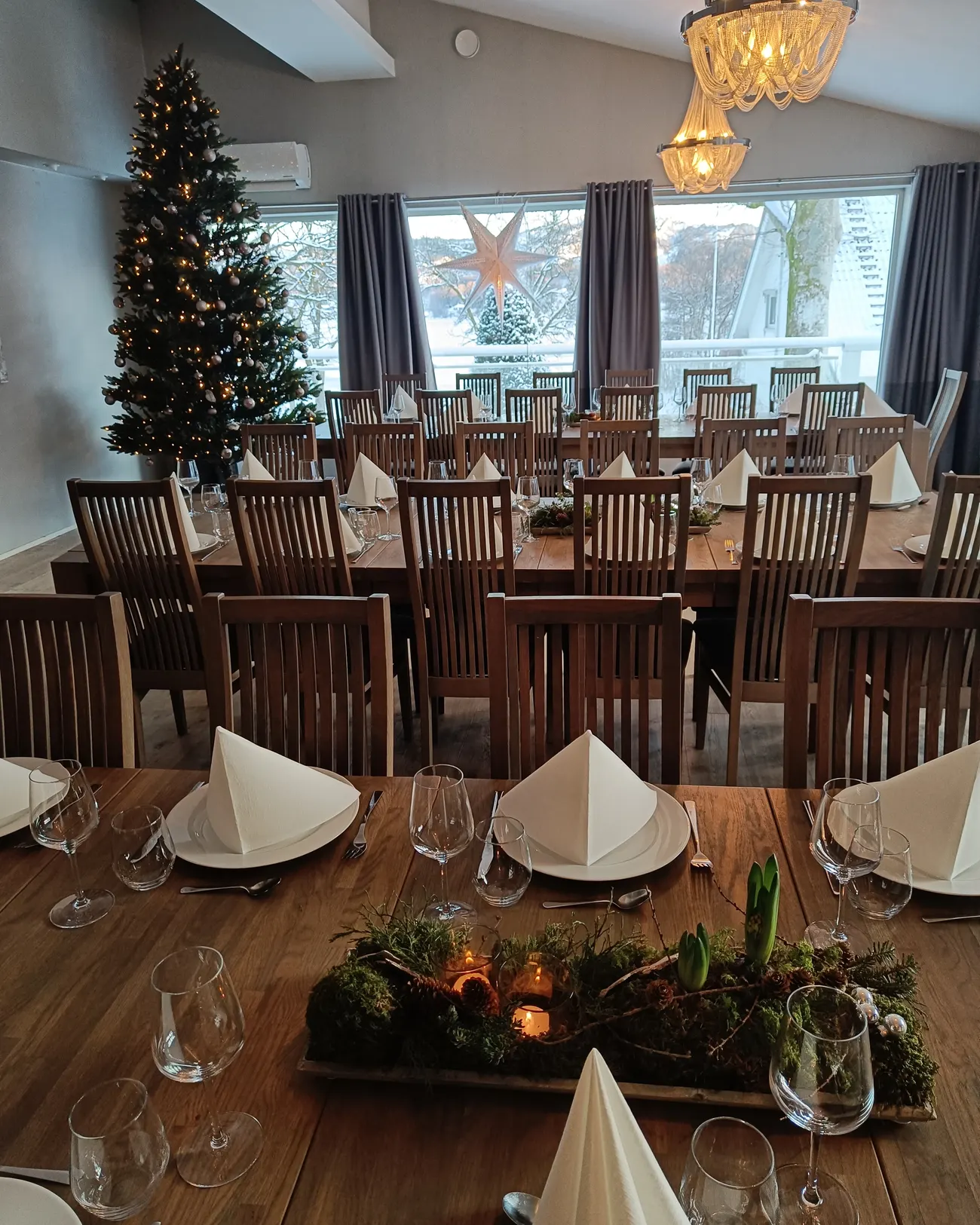 Spisesalen julepyntet med juletre, lysekrone og snø utenfor vinduene